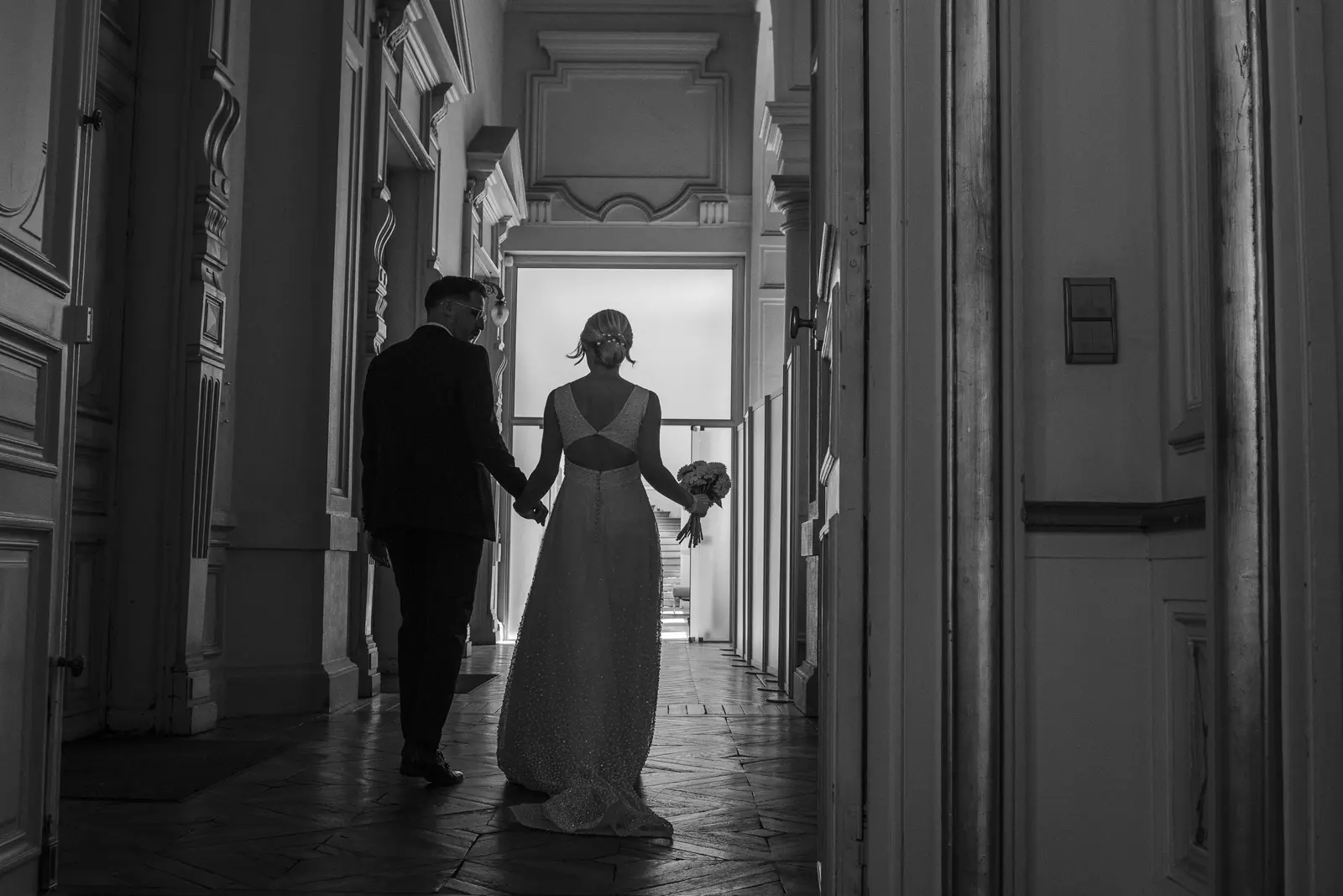 Les mariés main dans la main dans un couloir, en noir et blanc